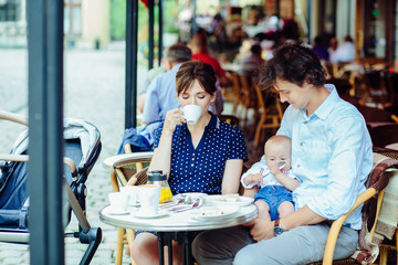 Fototapeta na wymiar young happy family of mother, father and newborn baby boy having breakfast in the street cafe in summer time
