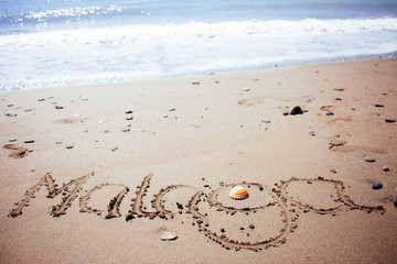 malaga handwritten in the sand with a shelfish
