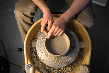 Hands of pottery artist work with earthenware on pottery wheel with raw clay. close up top view.