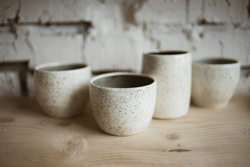 Glazed white ceramic rustic cups on wooden shelf in pottery workshop