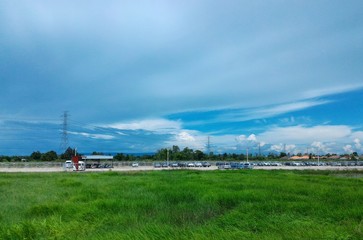 car park beside green rice field under cloudy blue sky