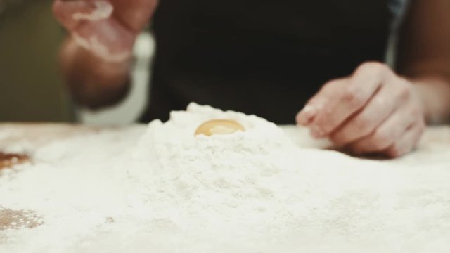 Woman baker putting yeast into flour heap in the kitchen. Concept of bakery and healthy nutrition. 