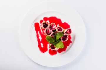 rolled pancakes stuffed with berries called white plate on a light background (close)