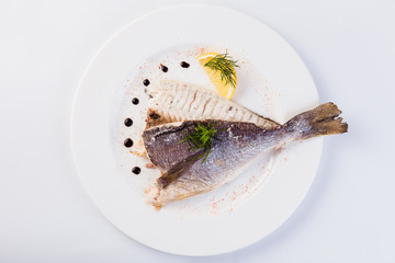 grilled dorada in salt with lemon slice on a white plate on a light background (close)