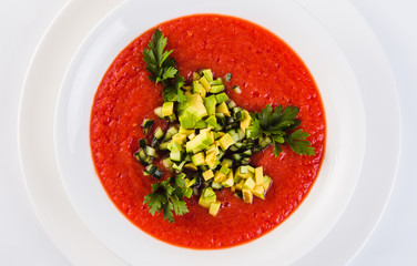 Spanish soup gazpacho with avocado and cucumber on a white plate on a light background