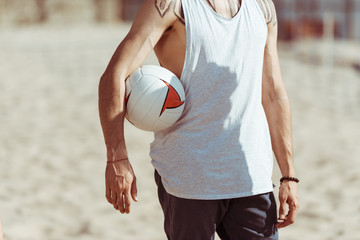 cropped view of man holding volleyball ball while standing on beach