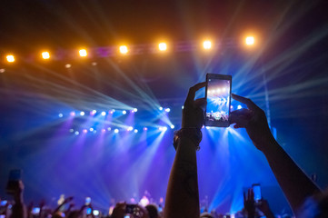 People in the crowd at a concert make video recordings and pics on a smartphone of published in social networks