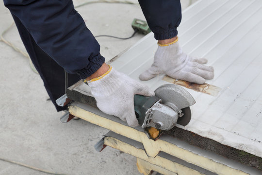 Cutting of heat insulated galvanized corrugated sandwich roof or wall panel, worker use angle grinder tool