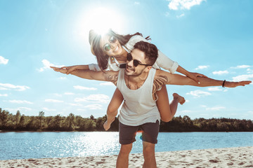 happy couple piggybacking while spending time on beach on summer day