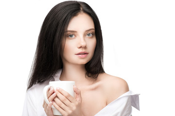 Gorgeous young woman holding cup with hot beverage and looking at camera