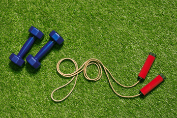 top view of dumbbells with jump rope in shape of word go on the grass