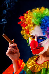 Mad clown on black background. Woman is smoking cigar. Portrait of crazy sad female with angry look...