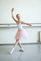 Cute little ballerina in pink ballet costume and pointe shoes is dancing in the room. Kid in dance...