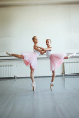 Fototapeta na wymiar Cute little ballerinas in pink ballet costume and pointe shoes is dancing in the room. Kid in dance class. Child girl is studying ballet. Copy space.
