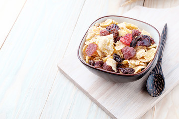 cornflakes and dry berry fruits in a brown bowl on a wooden background.