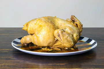 Closeup a chicken baked in a plate on the wood table.