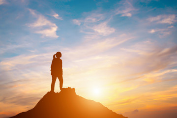 Silhouette of woman standing on hill in sunset.