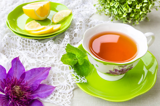 Herbal tea with a slice of lemon and a sprig of aromatic mint on a tablecloth in a rural style and a flower clematis. The concept of a romantic morning breakfast in the summer