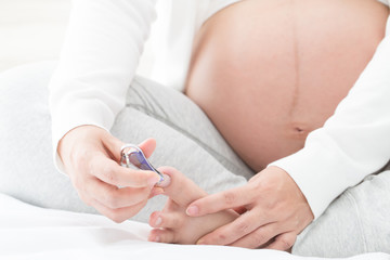 Pregnant woman cutting nails using nail clipper