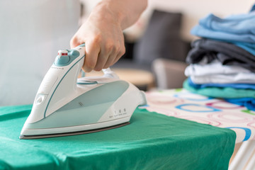 Iron on an ironing board with a green shirt close up from the side