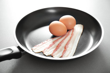 Frying pan with raw eggs and bacon on table