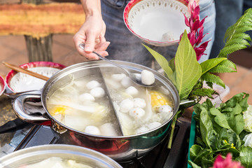 Hand adding ingredient into Asian steamboat pot meal