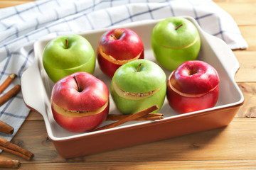 Fresh stuffed apples with cinnamon in baking dish on wooden table