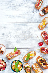 Fototapeta na wymiar Variety of sweet italian crostini with ricotta and fresh fruits. Small toasts with cream cheese and cut pear, peach, cherry and fig on white table with copy space.
