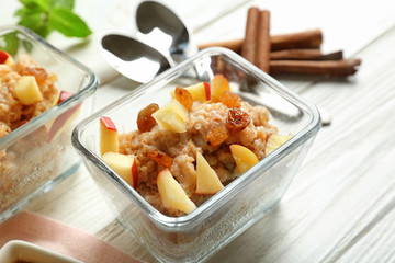 Glass bowl with oatmeal porridge, apples and cinnamon on light wooden table, closeup