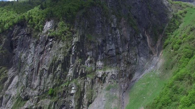 Panorama of the majestic rocky wall, cut by waterfalls and covered with green trees. Magic landscape in the mountains. Aerial view.
