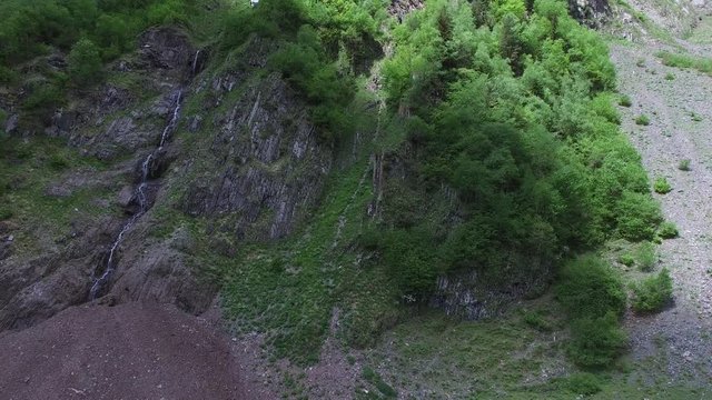 Flight over an extended waterfall, over a majestic rocky wall. The stream of water flows among the rocky slopes covered with green trees.