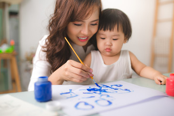 Happy family mother and daughter together paint. Asian woman helps her child girl.