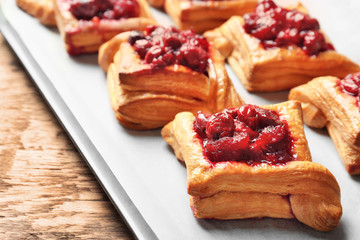 Tray with delicious puff pastries and cherry on wooden table