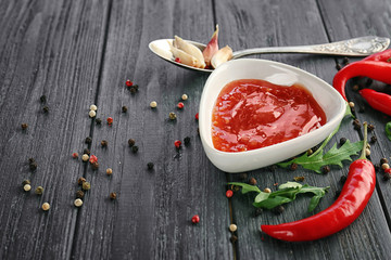 Composition of tasty chili sauce in bowl and ingredients on wooden table