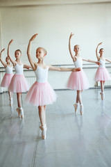Cute little ballerinas in pink ballet costume and pointe shoes is dancing in the room. Kid in dance class. Child girl is studying ballet. Copy space. - obrazy, fototapety, plakaty
