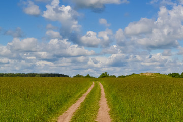 Country road through the field. Sky with clouds