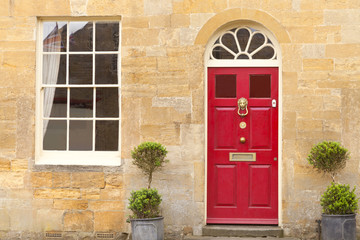 Red wooden doors in an old traditional English stone cottage with two plant pots in front .