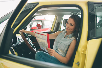 The young dark-haired woman examining car at the dealership and making his choice. Horizontal...