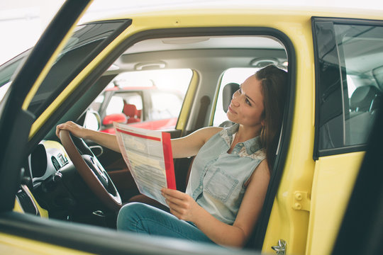 The young dark-haired woman examining car at the dealership and making his choice. Horizontal portrait of a young female model at the car. He is thinking if he should buy it