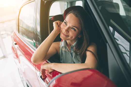 Closeup portrait happy, smiling, young attractive woman, buyer sitting in her new car isolated outside dealer, dealership lot office. Personal transportation, auto purchase concept