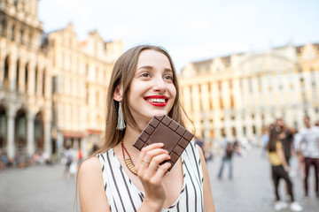 Obraz premium Young and happy woman with dark chocolate bar standing outdoors on the Grand place in Brussels in Belgium. Belgium is famous of its chocolate
