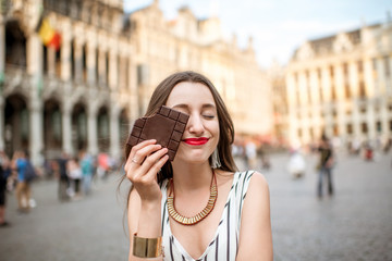 Young and happy woman with dark chocolate bar standing outdoors on the Grand place in Brussels in...
