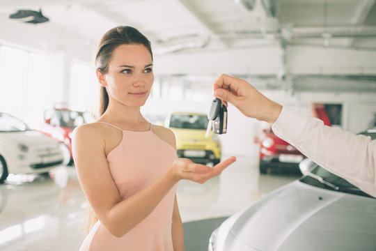 Woman Driver Holding Car Keys. Car Showroom. Seller or car salesman and female client 