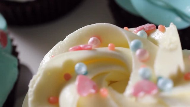 Sliding camera shooting. Close-up of blue and white cream on mafin. Icing sugar being sieved on pink frosted cupcake in slow motion