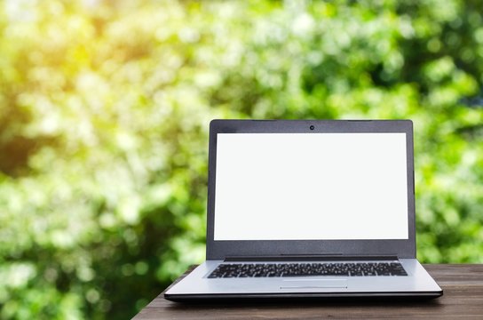 Laptop computer with white blank screen on wooden table with blurred nature green bokeh background, selective focus, copy space, business working outdoor, online social media, searching data concept