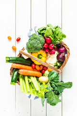 Colorful organic spring vegetables in wicker basket on wood - obrazy, fototapety, plakaty