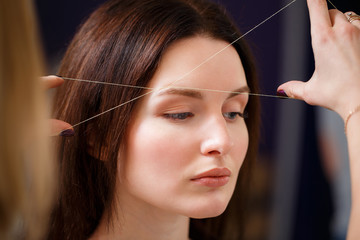 Cosmetologist plucks client eyebrows by thread