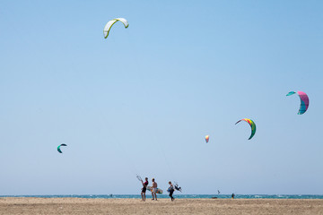 People practicing Kitesurfing. Beach on the peninsula Prasonisi, Rhodes. Colorful kites on the sea shore. Blue sea and windsurfing.