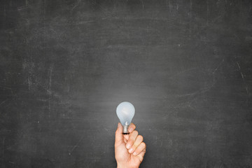 Businessman Holding Light Bulb Against Blank Blackboard