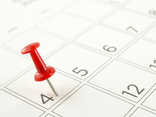 close-up single red plastic push pin tacking in 4th of july on schedule grid of desk calendar page,...